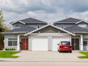 Large, mansion home with two white garage doors and a red sedan parked in the driveway